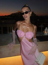 Woman in a pink dress with floral details and gloves at sunset.